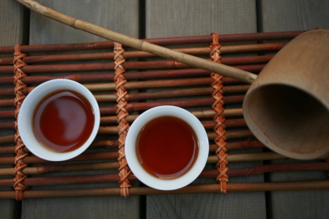 Two small cups of tea side by side on a woven bamboo mat